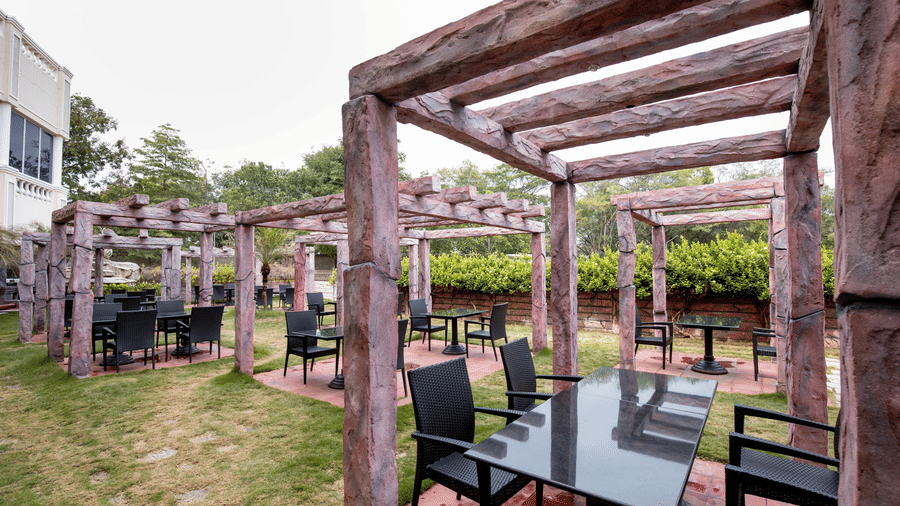 A scenic outdoor dining area with wooden pergola structures and black dining chairs in a garden setting - Jenneys Residency, Coimbatore