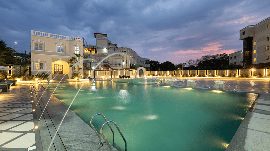 Outdoor swimming pool illuminated at dusk with water fountain jets spraying into the pool at Jenneys Residency.