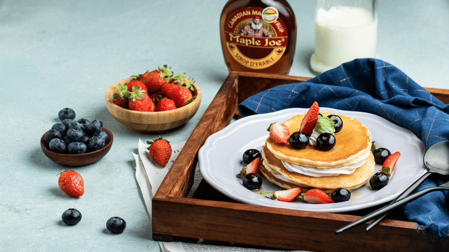 A stack of fluffy pancakes topped with fresh strawberries and blueberries served with maple syrup - Jenneys Residency, Coimbatore
