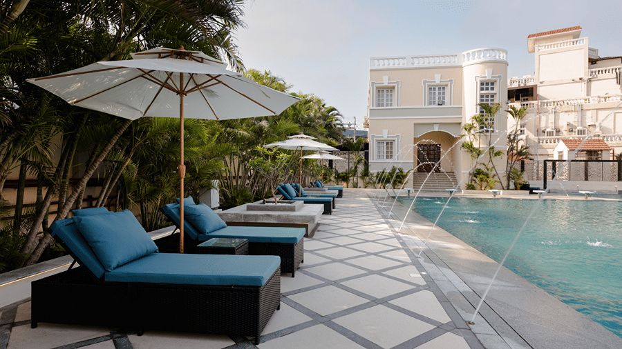Poolside relaxation area featuring cushioned sun loungers, shade umbrellas, and a calm pool deck at Jenneys Residency.