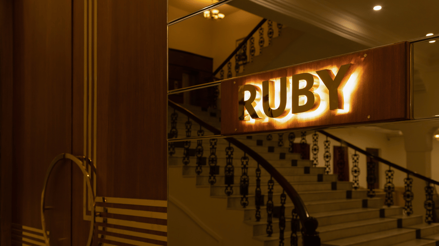 A view of the staircase leading up to the Ruby hall featuring prominent golden branding on the wall - Jenneys Residency, Coimbatore