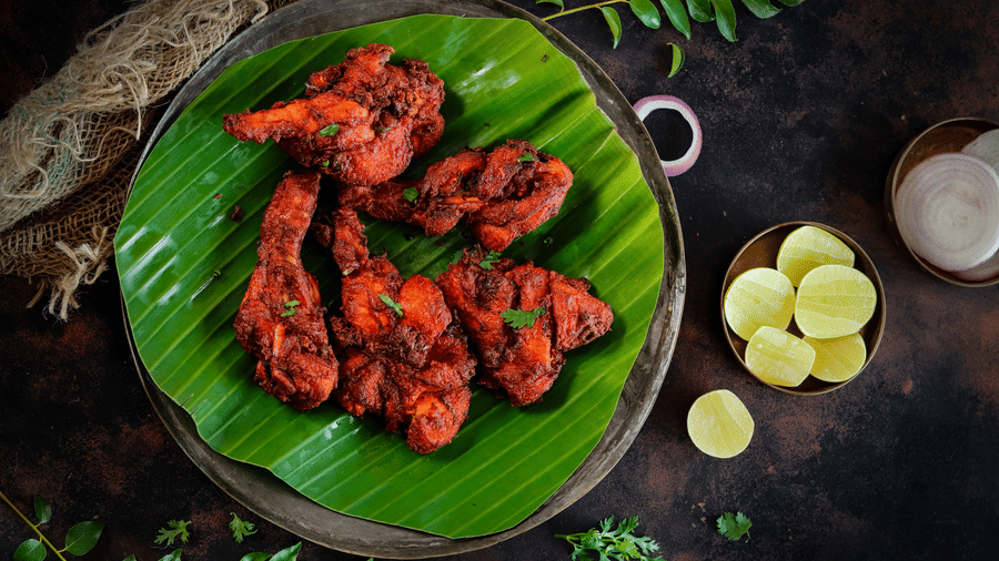A vibrant plate of spicy grilled chicken kebabs served on a green banana leaf with side accompaniments - Jenneys Residency, Coimbatore