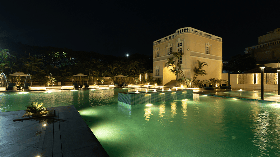 Night view of a swimming pool glowing with underwater lights in front of an illuminated hotel building at Jenneys Residency.