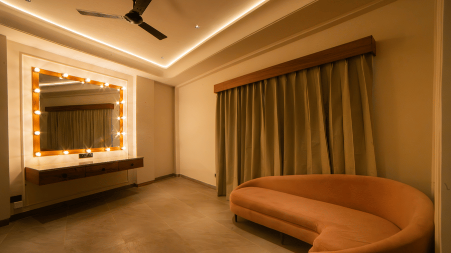 A suite featuring a curved orange sofa and a large vanity mirror framed by light bulbs, set against a backdrop of neutral walls and curtains at Jivana Wellness Retreat, Bhopal.