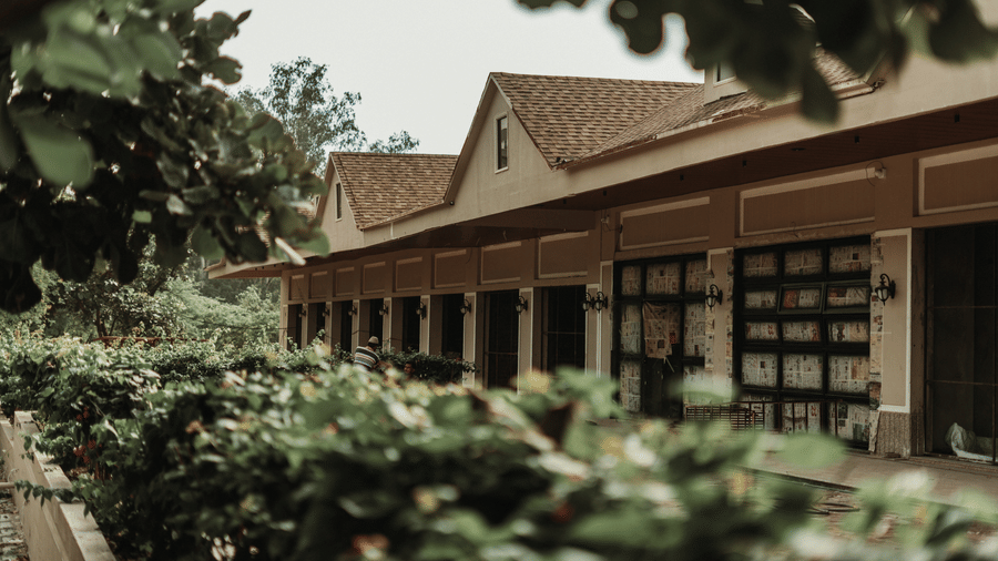 A house with a tiled roof and extended front section, seen beyond a garden with plants and a pathway running along the side at Jivana Wellness Retreat, Bhopal.