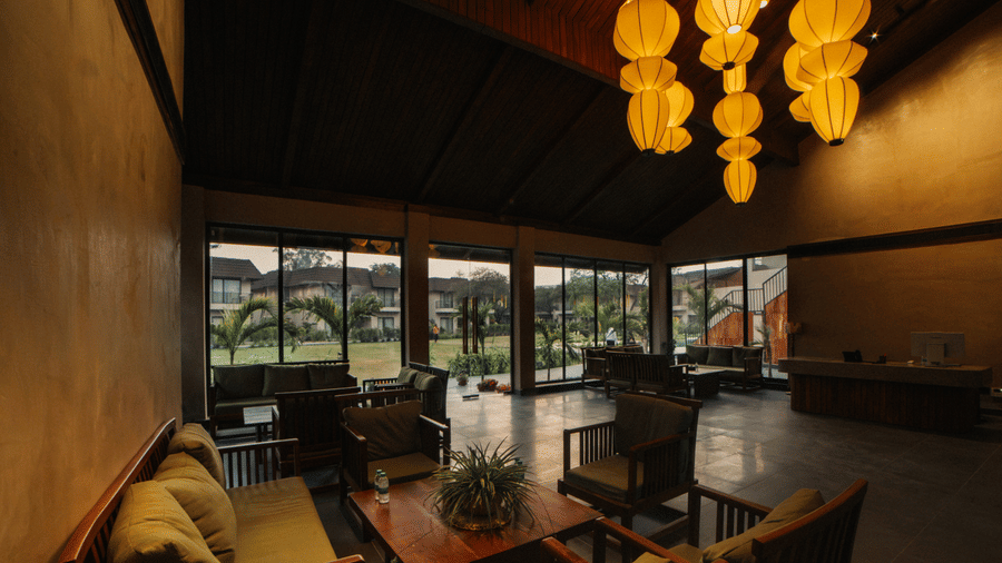 A lounge features wooden chairs with cushions, a coffee table, and large yellow lanterns hanging from a dark, high-sloped ceiling at Jivana Wellness Retreat, Bhopal.
