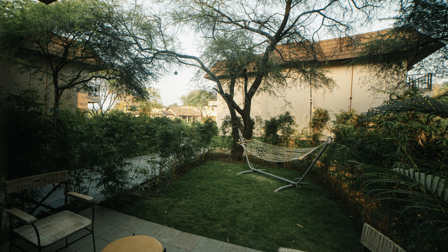 A sloped roof building with glass windows is surrounded by small palm trees and a flat grass lawn at Jivana Wellness Retreat, Bhopal.