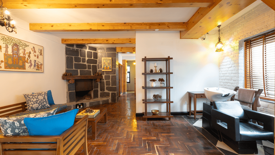 A warm lounge area featuring blue cushions, wooden beams, and a stone-clad fireplace.