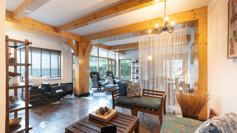 A bright common area with comfortable wooden furniture, floor-to-ceiling windows, and mountain views - Johnson Lodge & Spa, Manali