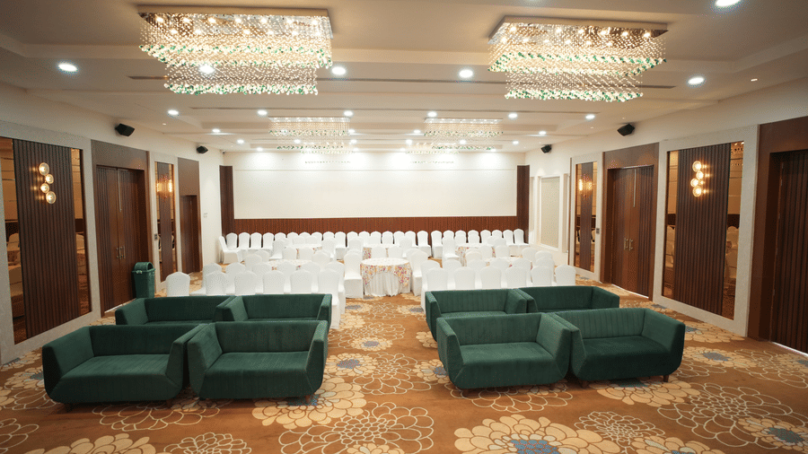 side view of a banquet hall at Kadamb Kuteer, Vrindavan featuring sofas, chairs and chandeliers. 