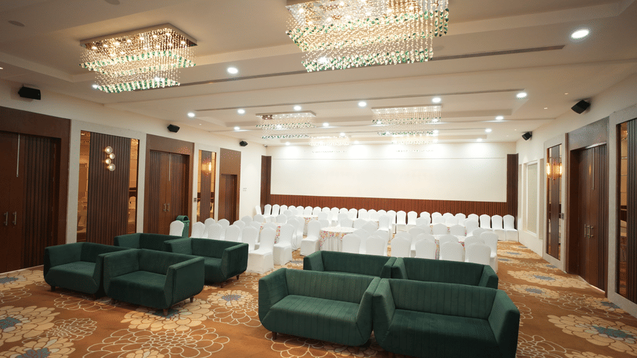 Overview of a banquet hall at Kadamb Kuteer, Vrindavan featuring sofas, chairs and chandeliers. 