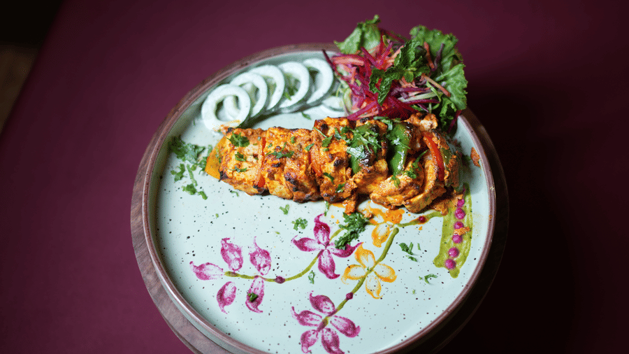 A gourmet vegetarian dish served on a white patterned plate at Kadamb Kuteer, garnished with fresh greens and colorful edible flower petals.