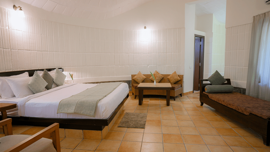 A cottage suite featuring a king size bed, sofa set, and daybed with patterned cushions at Kadkani River Resort, Coorg.