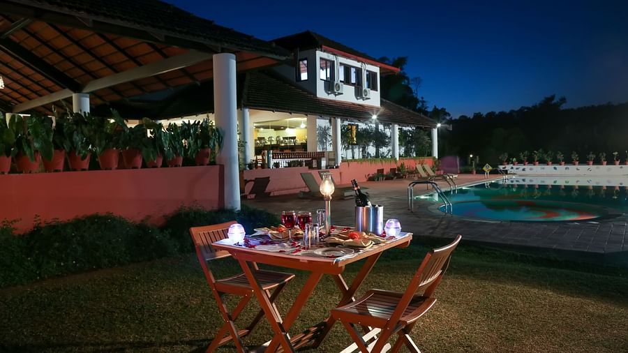 a view of a poolside dining setup with the resort in the background with a canopy on the left - Kadkani River Resort, Coorg