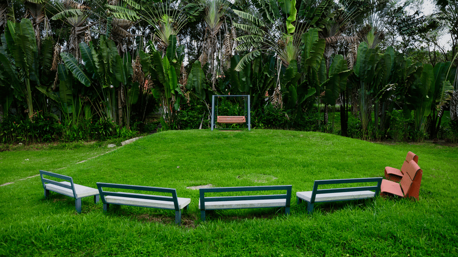 Grassy lawn featuring 4 bench seats arranged in an arc facing a swing set against a backdrop of trees at Kadkani River Resort, Coorg.