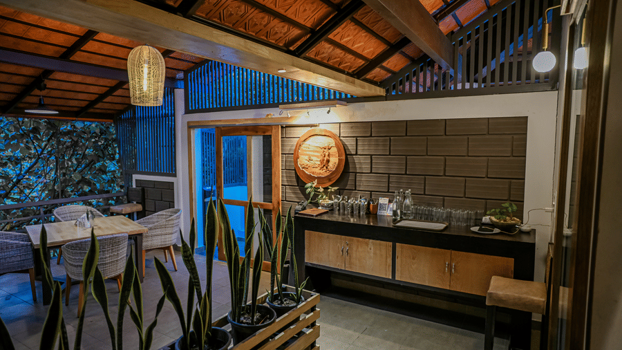 Indoor area with a wooden cabinet counter, potted plants, a circular wall decoration, and dining tables at Kadkani River Resort, Coorg.