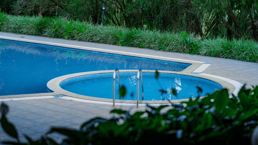 A small circular kids swimming pool built into a paved deck next to a larger pool, surrounded by green shrubs at Kadkani River Resort, Coorg.
