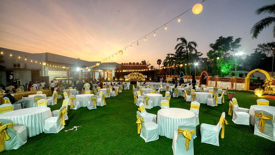 Outdoor event setup with banquet seating under decorative lights during dusk at Kailash Conventions ECR.