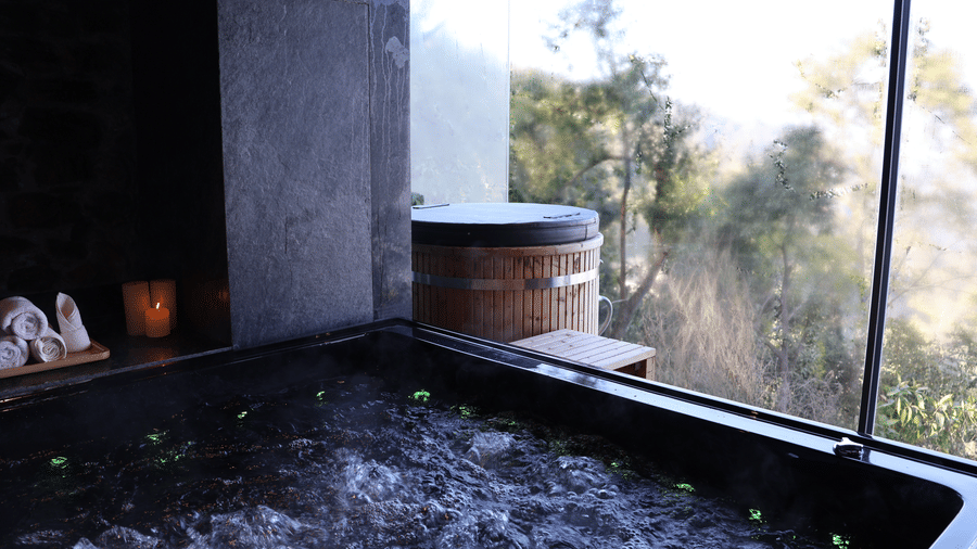 A bathing tub with water boiling next to a window which provides views of the outdoor.