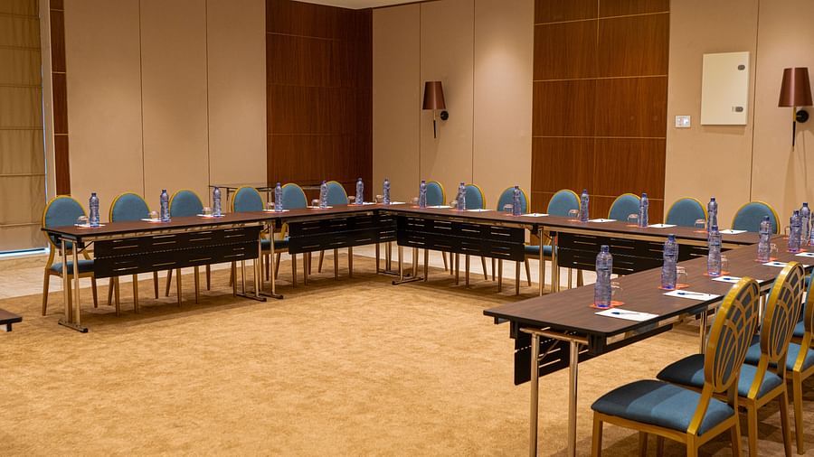 A conference room at KertelSuites with a U-shaped arrangement of tables and chairs, each table set with bottled water and notepads, in a well-lit, carpeted space
