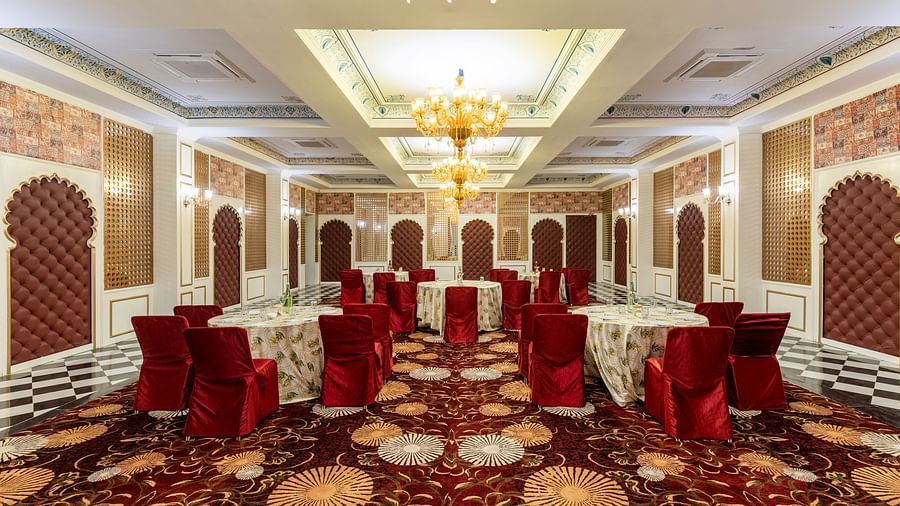 Luxurious banquet hall with red chairs and ornate ceiling at Kesar Bagh Palace.