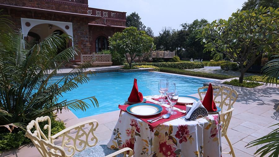 A poolside dining setup with floral tablecloths and chairs beside the heritage building - Khas Bagh, Jaipur.