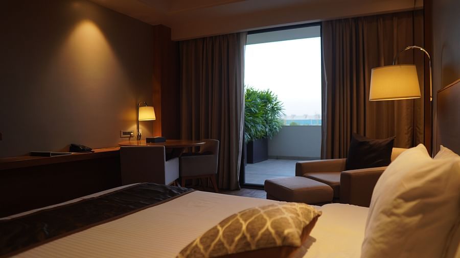 Large bed with soft lighting, comfortable cushioned seating, and a doorway leading to the balcony