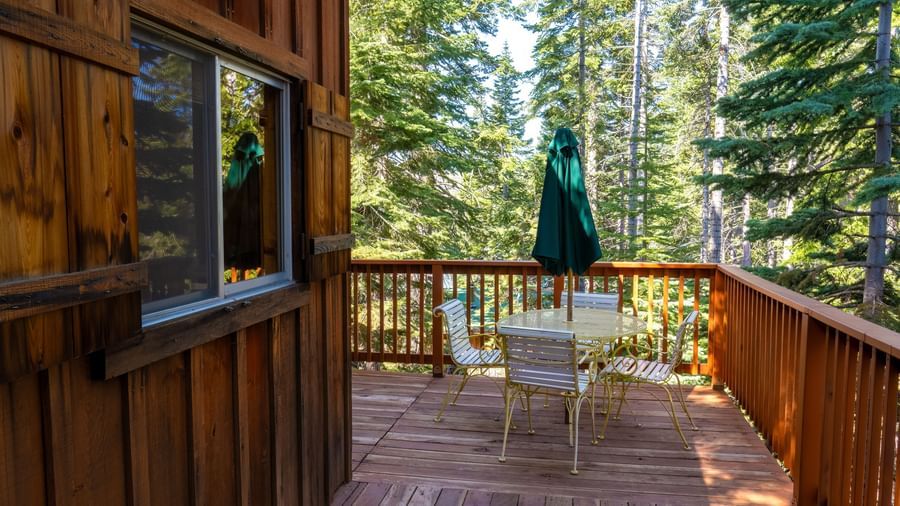 Wooden deck with table and chairs surrounded by tall pines outside a cabin at Kit Carson Lodge.