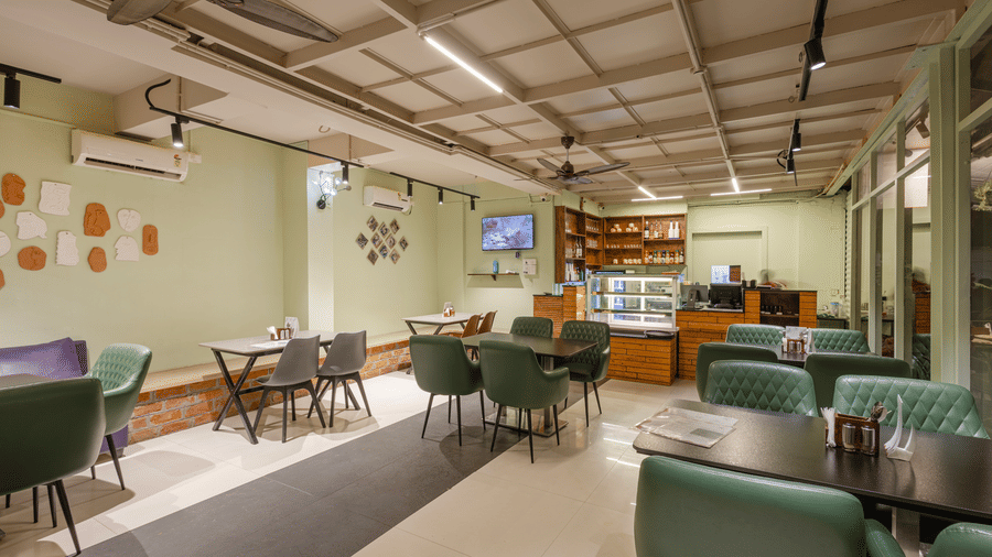 Indoor dining area of Claysutra Pottery Studio And Cafe at Kove Smart Stays that is furnished with multiple dining tables, a display case, and ample lighting.