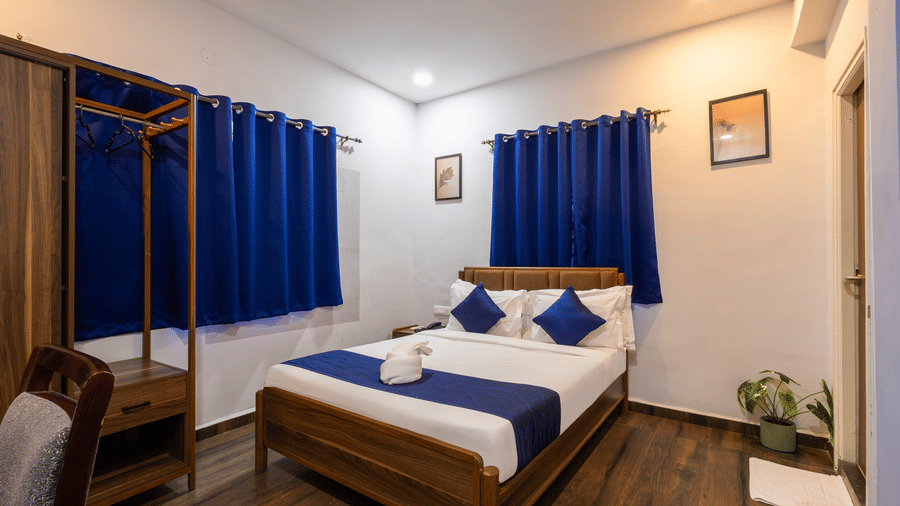 Wide view of the Deluxe Room at Kove Smart Stays highlighting the plush queen size bed, wooden flooring, closed curtains, and ample overhead lighting.