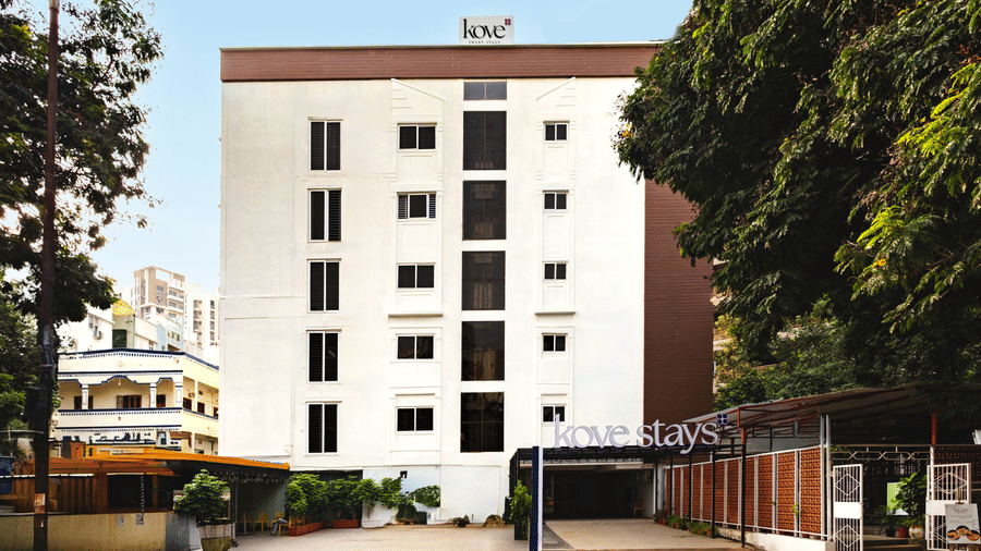 Facade of Kove Smart Stays seen on a bright day with a multi-storey structure, extended portico, and empty space in the front for parking.