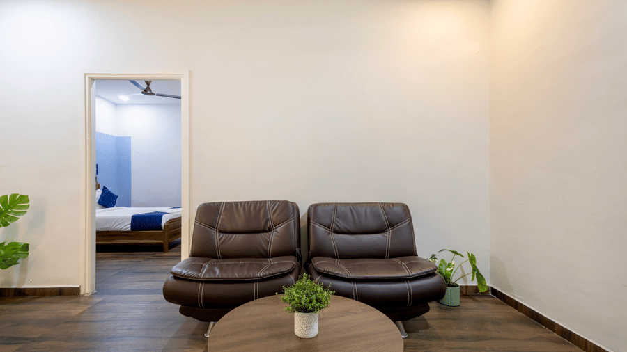 Spacious and separate living room in the Studio Room of Kove Smart Stays furnished with a multi-seater sofa with centre table, potted plants, and an entryway leading to the bedroom.