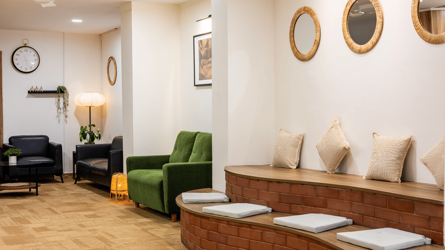 Seating area featuring wooden flooring, ample overhead lighting, and multiple upholstered sofas with cushions seen in the lobby of Kove Smart Stays, Hyderabad.