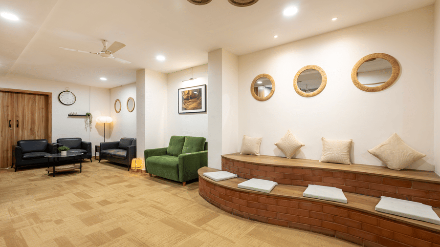 Extended view of the seating area featuring wooden flooring, ample overhead lighting, and multiple upholstered sofas with cushions seen in the lobby of Kove Smart Stays, Hyderabad.