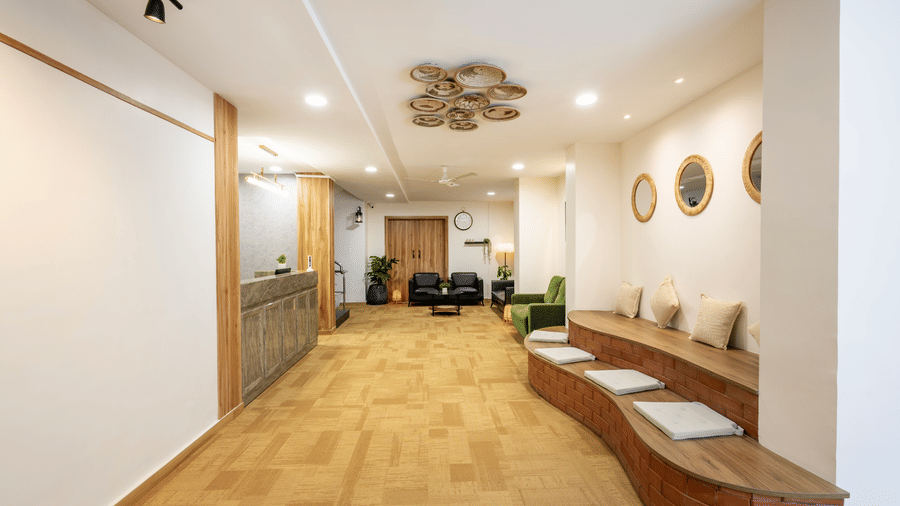 View of the seating area with cushions, in the lobby of Kove Smart Stays, facing the reception desk of the hotel under ample overhead lighting.
