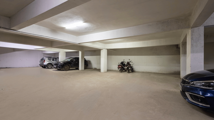 Wide view of the indoor parking of Kove Smart Stays seen with few parked vehicles and overhead lighting.