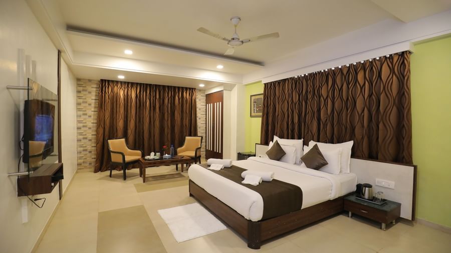 A spacious bedroom at Krushnai Resort featuring a king size bed, wall-mounted TV, and brown drapes.
