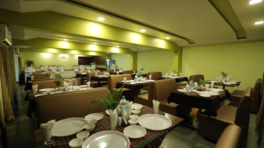 Dining setup at Krushnai Resort with round tables and brown chairs, plates and glasses on the table.