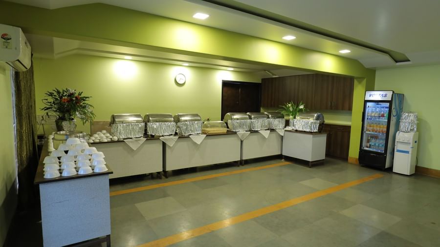 Buffet counter at Krushnai Resort with white dishes stacked and a beverage refrigerator in the background.