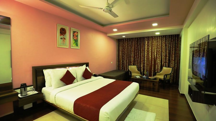 A bedroom at Krushnai Resort featuring a bed with a red runner, a flat-screen TV, and warm lighting.