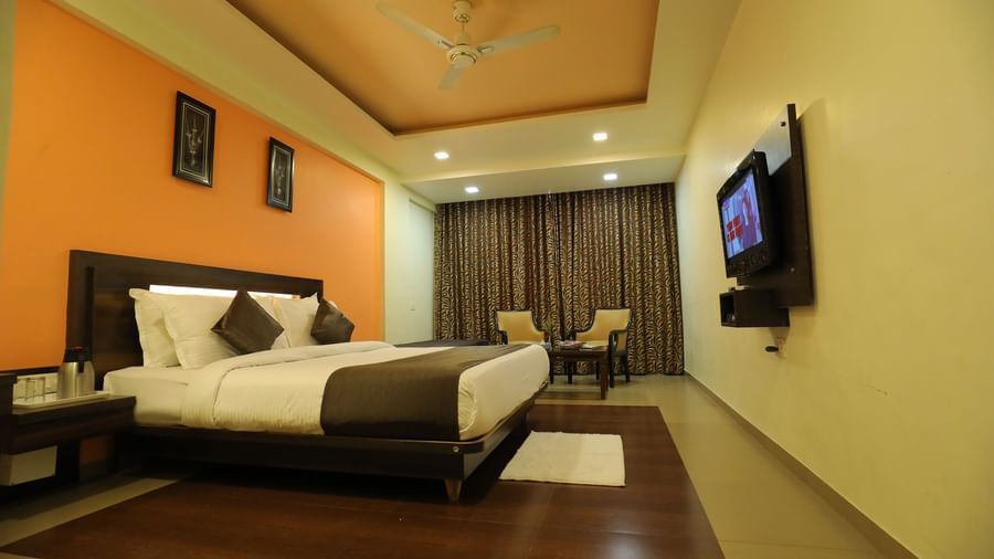A spacious bedroom at Krushnai Resort with a bed, an orange wall, and a large TV mounted on the wall.