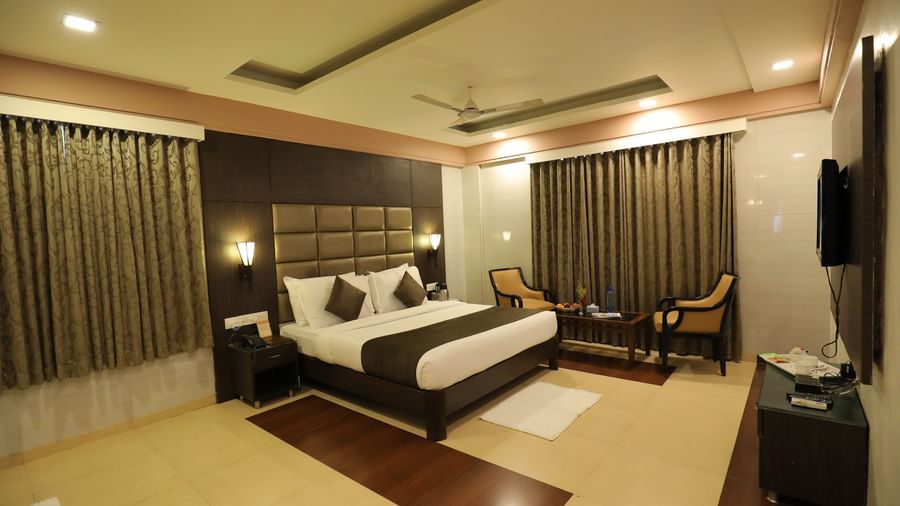 A front angle view of a bedroom at Krushnai Resort with a king size bed, a dark headboard, and brown drapes.