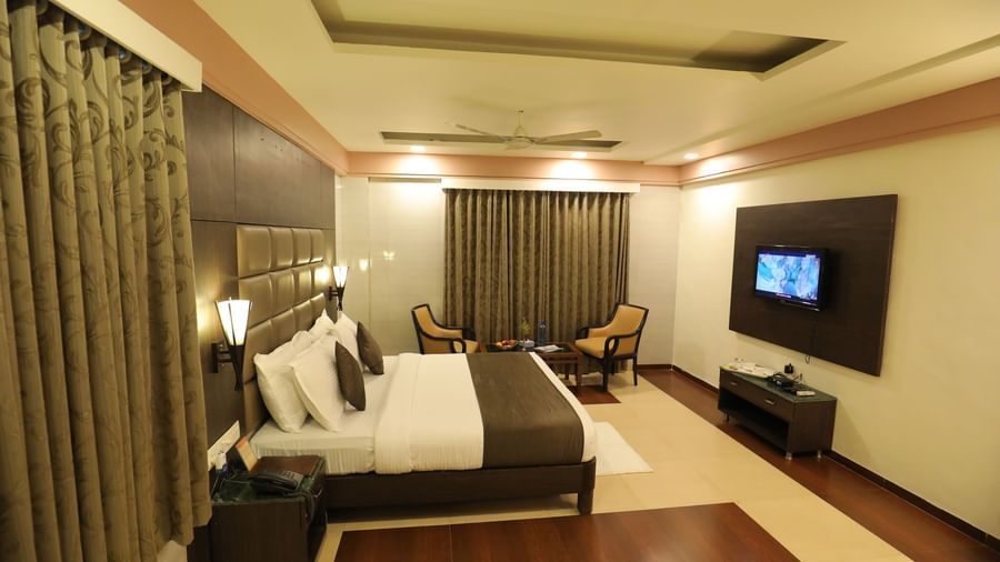 A wide view of a bedroom at Krushnai Resort with a large bed, lounge chairs and large windows with drapes closed.