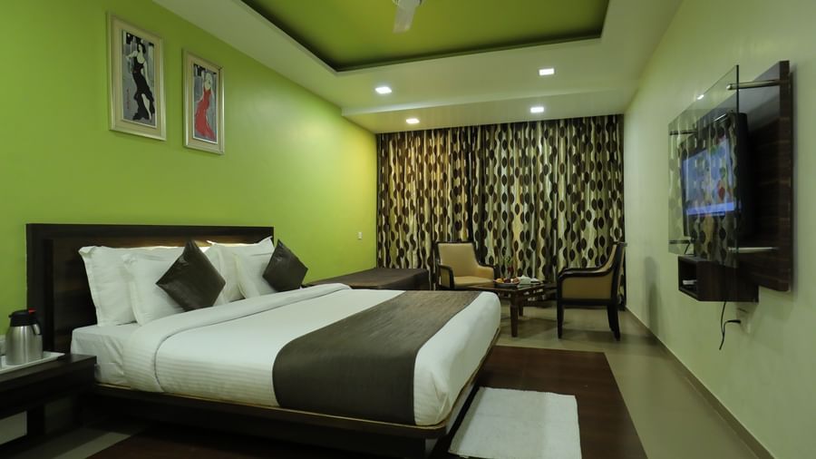 A bedroom at Krushnai Resort with a bed, green and white walls, and a flat-screen TV opposite the bed.