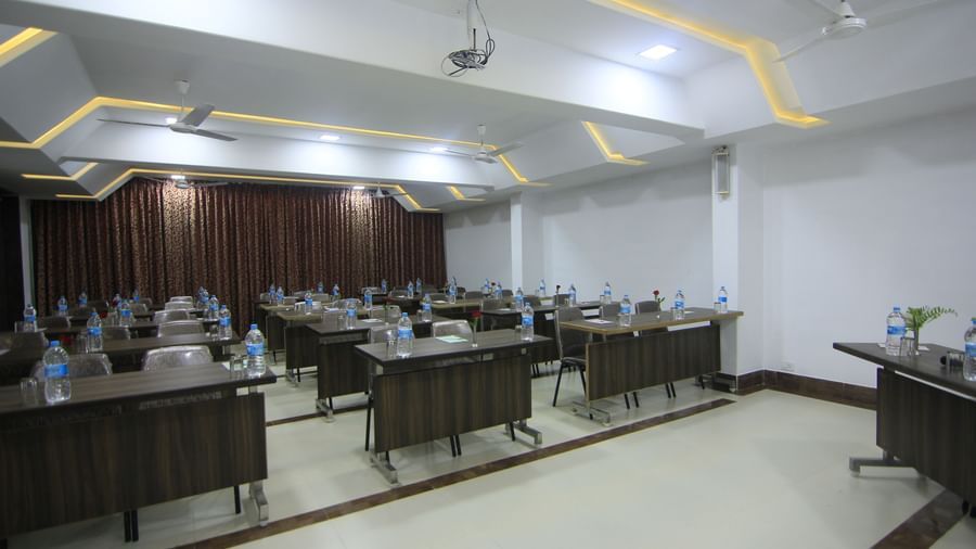 Conference room at Krushnai Resort with long rectangular tables arranged in class room style with chairs around them and a water bottle on each table.
