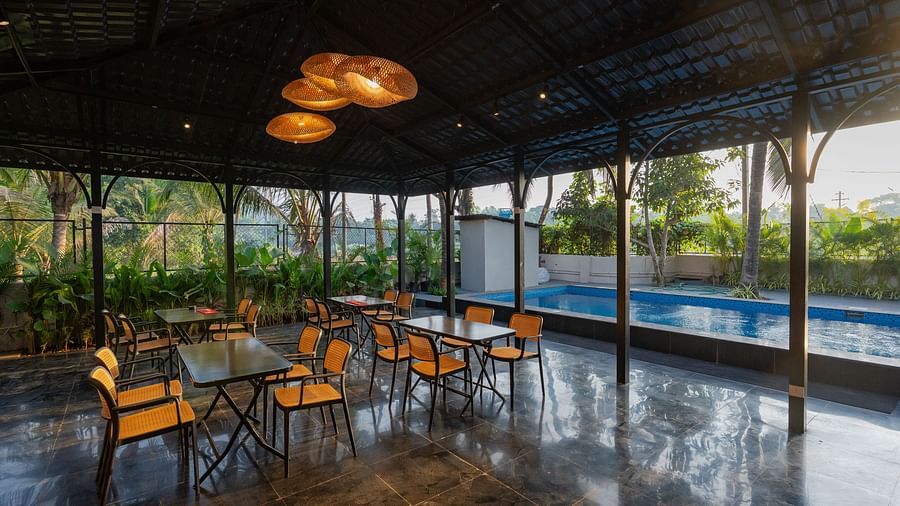Covered open-air dining area with tables and chairs, overlooking a swimming pool and lush greenery at Kssemya.