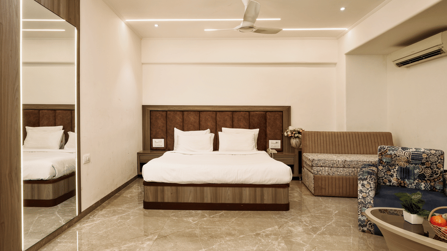 Full view of a suite showing the double bed, a sofa seating area, and mirrored wall panels, making the room appear larger at Kumar Resort by Turtle.