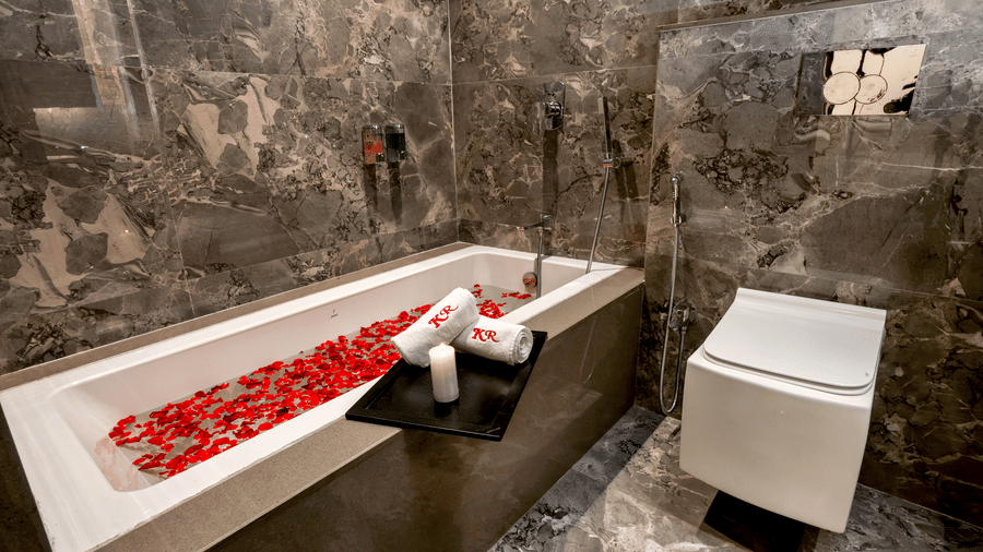 A deep bathtub filled with water and floating petals, positioned against a textured stone wall finish at Kumar Resort by Turtle.