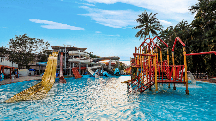 Wide view of the outdoor water park, showing a large water slide structure leading into a swimming pool at Kumar Resort by Turtle.