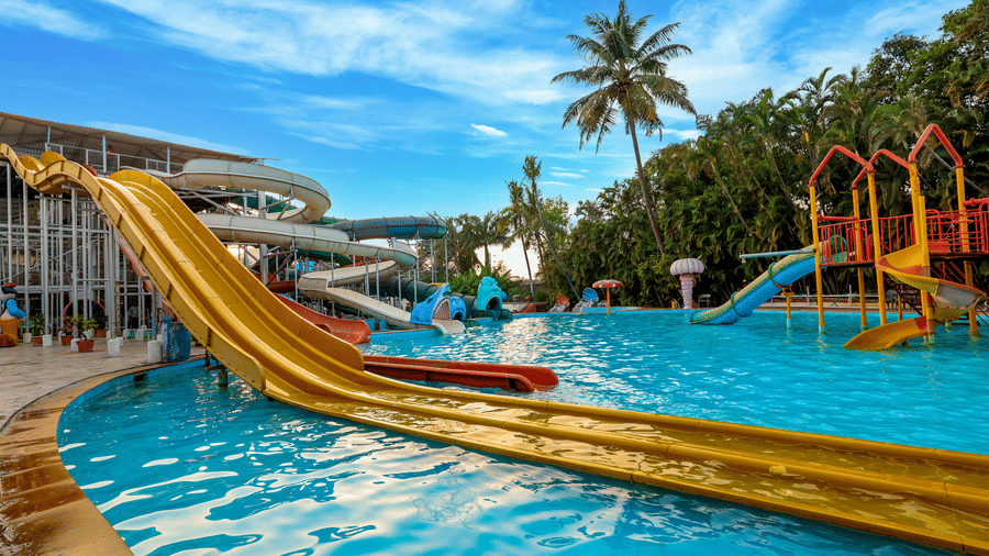 Water park scene featuring a long, wide single-lane slide emptying into the shallow pool under a bright sky with palm trees at Kumar Resort by Turtle.